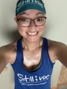 Laura taking a sweaty, after run selfie sporting their Still I Run headband and blue tank top.